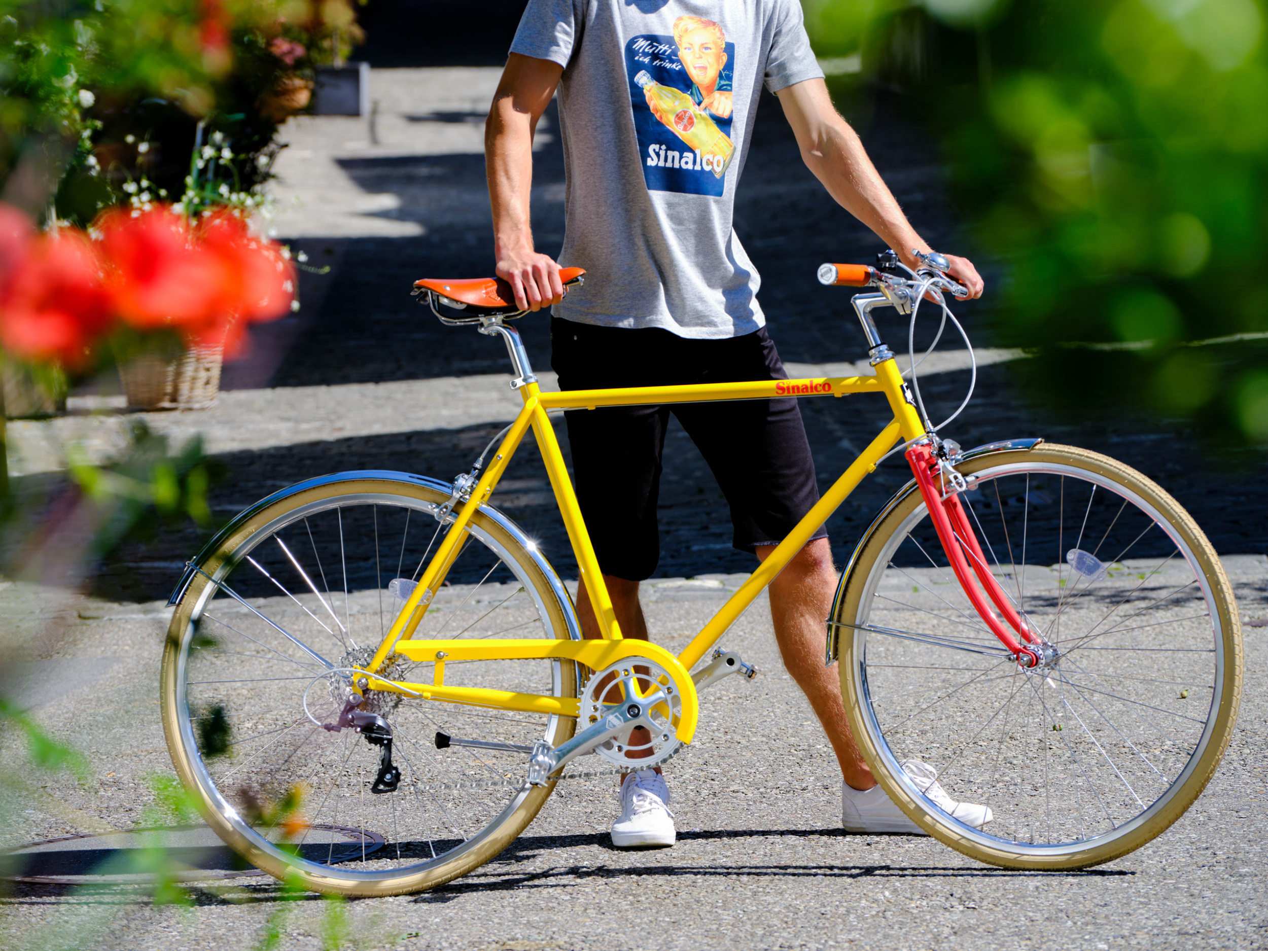 Ein Mann mit Sinalco T-Shirt schiebt ein Sinalco Fahrrad